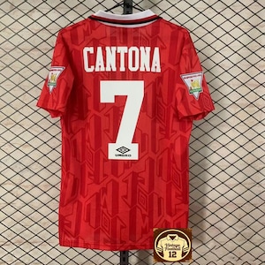 May include: A white ceramic mug with a black handle and the text "But First, Coffee" in a black, handwritten-style font. The mug is on a white surface.