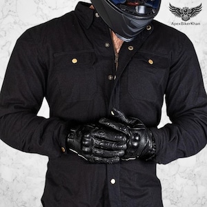 May include: Black button-down shirt with gold buttons and a zipper. The image also shows black leather motorcycle gloves. A black motorcycle helmet is visible in the background. The text "ApexBikerKhan" is in the upper right corner.