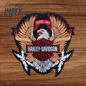 May include: Embroidered Harley-Davidson patch featuring a central eagle with outstretched wings, the text "HARLEY-DAVIDSON CYCLES" and "SINCE 1903". The patch has a black background with red, white, and gold accents. The patch is on a wooden surface.