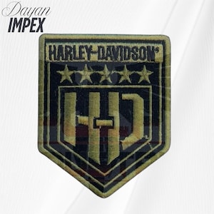 May include: A black and gold Harley-Davidson patch with the brand name and five stars embroidered on it. The patch has a shield shape with the letters "HD" in the center. The text "Dayan Impex" is in the upper left corner.
