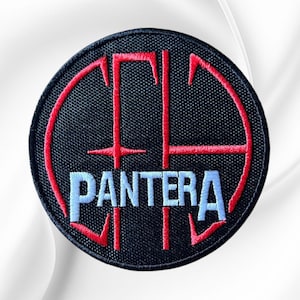 May include: A circular embroidered patch with a black background. It features a red stylized cross design overlaid with the word PANTERA stitched in light blue capital letters. The patch has a black stitched border around the entire circumference.