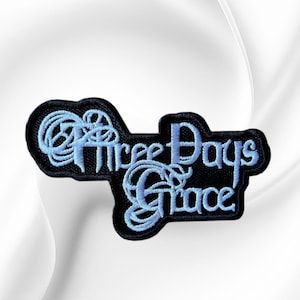 May include: A black embroidered patch featuring the text Three Days Grace in a light blue, stylized, cursive font. The patch has a dark border that follows the contour of the lettering, creating a distinct shape for the band logo design.
