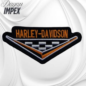 May include: Black and orange Harley-Davidson patch with the brand name in orange block letters. The patch has a black border and a white and orange geometric design. The patch is likely for a jacket or vest.