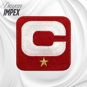 May include: Embroidered patch with a red square border, featuring a large white "C" and a gold star at the bottom. The text "Dayan IMPEX" is at the top left corner in a script font. This patch is likely for apparel or accessories.