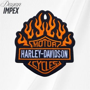 May include: Embroidered patch featuring the Harley-Davidson logo with orange flames on a black background. The text "MOTOR HARLEY-DAVIDSON CYCLES" is displayed in white. The patch has a black border and is likely for jackets or bags.