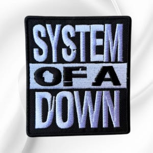 May include: A rectangular embroidered patch with a black background and white stitched lettering. The text reads SYSTEM in the top section, OF A in the middle section, and DOWN in the bottom section, all in a bold, block-style font.