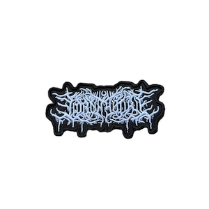 May include: A rectangular embroidered patch featuring a black background with intricate, light blue, stylized lettering that resembles tangled, dripping branches or roots. The edges of the patch follow the irregular, jagged outline of the text design.
