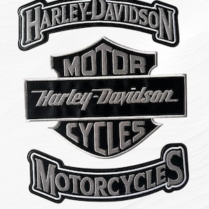 May include: Set of Harley-Davidson patches in black and silver. The patches include the Harley-Davidson logo, the words "MOTOR," "CYCLES," and "MOTORCYCLES." The patches are embroidered with a silver thread and have a black background.