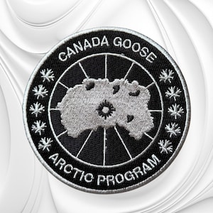 May include: A circular embroidered patch featuring a black background with a silver-grey map of the Arctic region in the center. The text CANADA GOOSE and ARCTIC PROGRAM are stitched in white along the border, accented by small maple leaf icons.