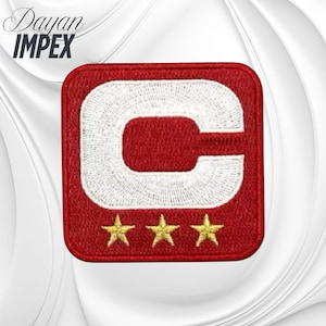 May include: Embroidered patch with a red square border, featuring a white letter "C" and three gold stars at the bottom. The text "Dayan IMPEX" is in the upper left corner, in a cursive font.