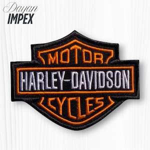 May include: Embroidered Harley-Davidson patch in black, orange, and white. The patch features the Harley-Davidson logo with the words "MOTOR HARLEY-DAVIDSON CYCLES" in a shield shape. The text "Dayan Impex" is at the top.
