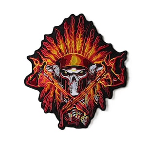 May include: An embroidered patch featuring a central skull wearing a headdress with vibrant red, orange, and yellow feathers. Two crossed axes are positioned in front of the skull, all set against a black background with a jagged edge border.