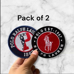 May include: Two embroidered patches with the text "POLO RALPH LAUREN" and "POLO EST. 1967". One patch features a red "P" with stars and stripes, the other a polo player. The text "Pack of 2" is above the patches.