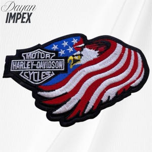May include: Embroidered patch featuring the Harley-Davidson Cycles logo, an American flag design, and an eagle. The patch has a black border, with red and white stripes, blue stars, and the text "MOTOR HARLEY-DAVIDSON CYCLES".