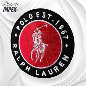 May include: Circular black patch with a red center featuring a white embroidered polo player logo. The patch is ringed with white text that reads "POLO EST. 1967" and "RALPH LAUREN". The logo is a classic equestrian design.