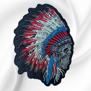 May include: An embroidered patch featuring a profile view of a human skull wearing a vibrant headdress. The headdress is composed of red, white, and blue feathers with a detailed blue and red headband. The patch has a dark navy blue background.