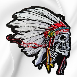 May include: An embroidered patch featuring a skull wearing a large white feathered headdress. The headdress includes red accents, a teal geometric band, and a yellow circular emblem. The skull is white with black shading, and red ribbons flow.