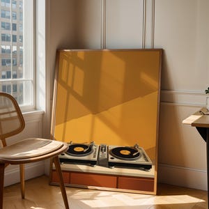 A large framed art print of vinyl turntables leans on the floor beside a wooden chair and sunlight-filled window.