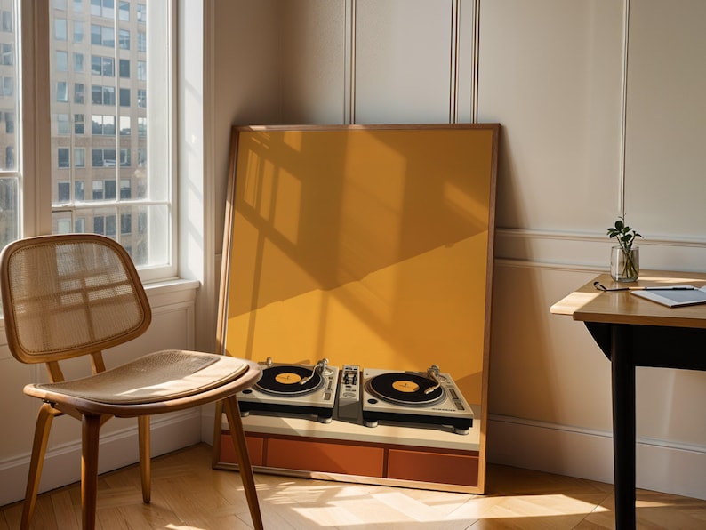 A large framed art print of vinyl turntables leans on the floor beside a wooden chair and sunlight-filled window.