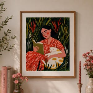 Puede incluir: Una lámina de arte enmarcada que representa a una persona de pelo oscuro con un vestido rojo de flores, sentada en hierba alta verde mientras lee un libro y sostiene a un gato blanco y naranja. La ilustración presenta follaje verde y detalles rojos.