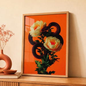 Puede incluir: Impresión artística enmarcada que presenta una serpiente roja oscura enroscada alrededor de flores blancas y amarillas sobre un fondo naranja vibrante. La obra de arte se muestra en un marco de madera natural, añadiendo calidez.