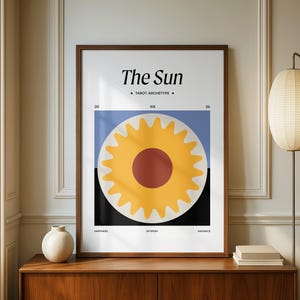 Puede incluir: Una impresión artística enmarcada con un diseño de sol amarillo y un centro rojo, sobre un fondo azul y negro. El texto "The Sun" y "Tarot Archetype" se muestran en la parte superior. La impresión se exhibe en un mueble de madera.