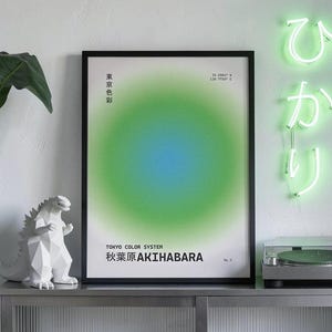 Puede incluir: Un póster enmarcado con un diseño de gradiente verde y azul, etiquetado como "TOKYO COLOR SYSTEM AKIHABARA". Una estatua blanca geométrica de Godzilla y un tocadiscos plateado se encuentran sobre un mueble metálico. Un letrero de neón verde con caracteres japoneses está montado en la pared.