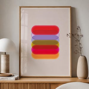 Puede incluir: Una lámina de arte mural enmarcada que presenta una pila vertical de seis formas de píldora translúcidas de bordes suaves en tonos vibrantes de rojo, morado, verde oliva, carmesí, magenta y naranja, sobre un fondo beige neutro y sólido.