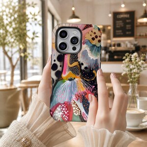 May include: A smartphone case featuring an abstract, multi-colored design with black, pink, yellow, and teal shapes, intricate white line work, and dotted patterns. The case has a cutout for a triple-lens camera system on the upper left corner.