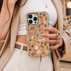 Peut inclure: Une coque de smartphone beige avec un motif répétitif de citrouilles orange, de glands marron, de feuilles d'automne aux tons orange et marron, et de petites tasses de café fumantes, le tout sur un fond marron clair.