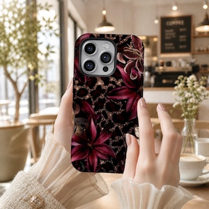 May include: A smartphone case featuring a dark background with a leopard print pattern and burgundy floral accents. The case has a glossy finish and a camera cutout. The design includes a mix of dark red and gold colors.