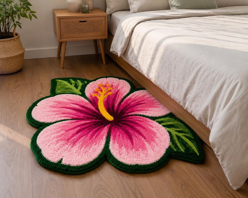 May include: A colourful, flower-shaped rug with a pink hibiscus design, yellow stamen, and green leaves. The rug is on a wooden floor near a bed, adding a tropical touch to the room's decor. The rug's dimensions are approximately 120 cm.