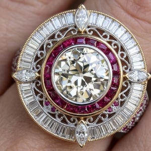 Op de afbeelding: Een sierlijke ring met een grote centrale diamant, omringd door robijnen en baguette-geslepen diamanten. De ring heeft een goud- en zilveren filigraanontwerp, aangevuld met marquise-geslepen diamanten. Een luxueus sieraad.