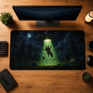 May include: A rectangular desk mat featuring a dark, nocturnal forest scene with a raccoon being abducted by a glowing green UFO beam. The graphic includes a full moon, silhouetted pine trees, a small cabin, and a vintage pickup truck in the background.