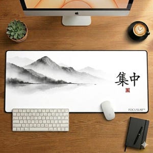 Könnte beinhalten: Ein rechteckiges weißes Mauspad mit schwarzem Rand zeigt ein schwarz-weißes Berglandschaftsdesign. Das Mauspad trägt den Text "集中" und "FOCUSLAB". Eine weiße Tastatur und Maus liegen auf dem Holztisch.