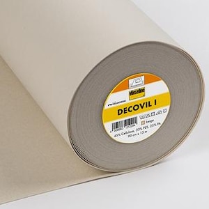 May include: A roll of beige Decovil I fabric. The label shows the brand name and product details. The fabric is partially unrolled, revealing the inner core. The roll is on a white surface.