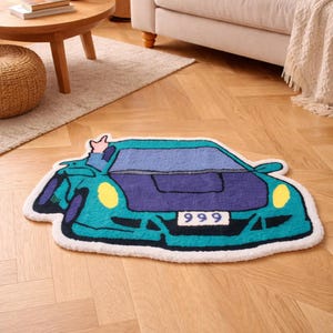 Può includere: Un tappeto a forma di auto turchese e viola con fari gialli e il numero "999" sulla parte anteriore. Il tappeto ha un bordo bianco ed è posizionato su un pavimento in legno.