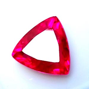 May include: A bright red, triangular gemstone with a clear, open centre. The gem is cut to catch the light, creating a sparkling effect. The edges are smooth and polished, giving it a refined appearance. A striking piece of jewellery.