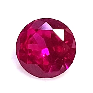 May include: A faceted, round-cut ruby gemstone. The gem is a deep, vibrant red color with multiple facets that reflect light. The gemstone is set against a white background, highlighting its color and clarity.