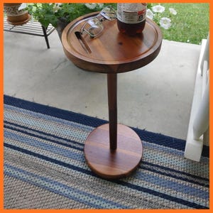 May include: A round, wooden side table with a dark finish. The table has a circular top with a groove and a single stem base. A pair of glasses and a bottle are on the table. The table is approximately 24 inches tall.