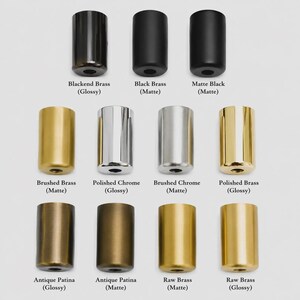 May include: A collection of twelve cylindrical metal knobs arranged in three rows. The finishes include Blackened Brass, Black Brass, Matte Black, Brushed Brass, Polished Chrome, Brushed Chrome, Polished Brass, Antique Patina, and Raw Brass.