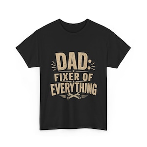 Könnte beinhalten: Schwarzes T-Shirt mit dem Text "DAD: FIXER OF EVERYTHING" in einem verblichenen, beigefarbenen Schriftzug. Das Design beinhaltet einen Schraubenschlüssel und einen Stern. Ein lässiges T-Shirt für den Alltag.