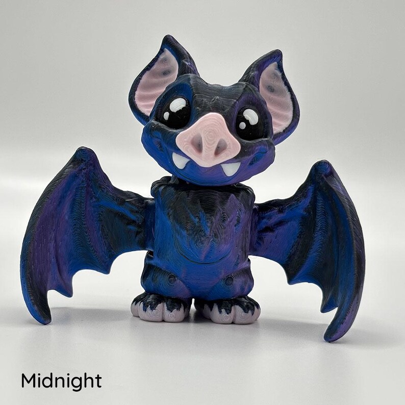 A 3D-printed Midnight coloured vampire bat fidget in shades of blue, black and purple, with little fangs. The bat has large, expressive eyes and is posed with its wings spread.