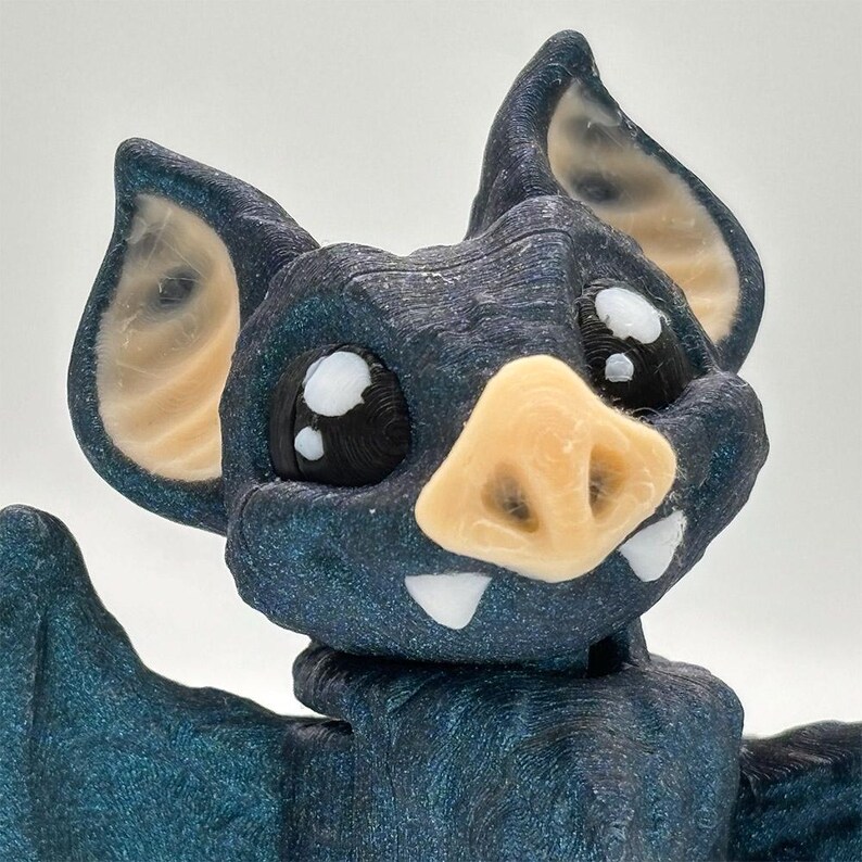 A detailed 3D-printed bat figurine. The dashing vampire bat is made with a glittery blue-black filament,  and has a charming fanged smile.