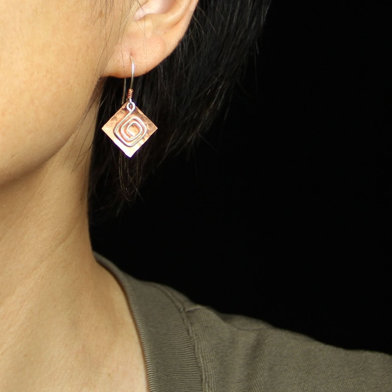 May include: A pair of copper earrings with a hammered finish and a spiral design. The earrings are silver in color and have a diamond shape.