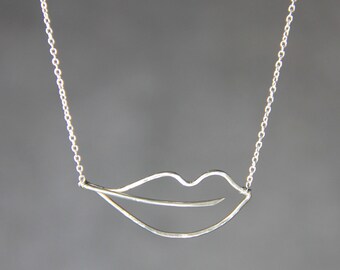 May include: A silver chain necklace with a simple, minimalist lip pendant.