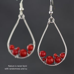 Pu&ograve; includere: Orecchini a forma di lacrima in argento con perline di corallo rosso che pendono all'interno.