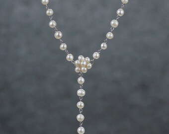 May include: A white pearl necklace with a cluster of pearls at the center and a single pearl drop.