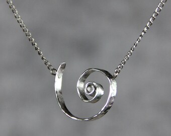 Puede incluir: Un collar de plata con un colgante en espiral martillado. El colgante está hecho de una sola pieza de metal que se retuerce en forma de espiral.