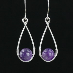 May include: A pair of silver dangle earrings with a purple amethyst gemstone in each. The earrings are made with a twisted wire design.
